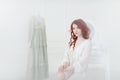 Tender portrait of a young dreamy redhead woman in nightdress. She is sitting in dress room and planning to wear beautiful vintage Royalty Free Stock Photo