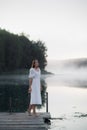 Tender romanitc sentimental female lady in the morning on a wooden pier near the misty river in a white dress Royalty Free Stock Photo