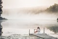 Tender romanitc sentimental female lady in the morning on a wooden pier near the misty river in a white dress Royalty Free Stock Photo