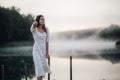 Tender romanitc sentimental female lady in the morning on a wooden pier near the misty river in a white dress Royalty Free Stock Photo