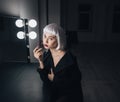 Tender woman in blonde wig applying lipstick near the mirror