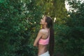 Tender young girl with brunette long hair dressed in pink bra stands among green bushes Royalty Free Stock Photo