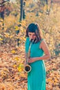 Tender young girl with dark hair in a beautiful long blue dress plays the alto saxophone in a yellow autumn park Royalty Free Stock Photo