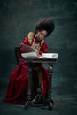 Tender young woman, medieval royal person sitting at table and writing letter against vintage green background. African Royalty Free Stock Photo