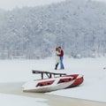 Tenderly hugging couple in the front of the snowy boat near the forest during the snowfall.