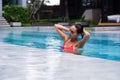 Tenned beautiful asian woman in orange bikini and sunlasses sitting in swimming pool. Fashionable portrait. Elegant Royalty Free Stock Photo