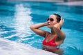 Tenned beautiful asian woman in orange bikini and sunlasses sitting in swimming pool. Fashionable portrait. Elegant Royalty Free Stock Photo