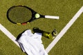 Tennis ball, racket, towel and water bottle lying on sunny outdoor grass tennis court Royalty Free Stock Photo