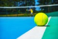 Tennis ball on white court line on hard modern blue green court with player, net, balls, trees on the background. Royalty Free Stock Photo