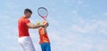 Tennis coach or instructor and child tennis player. Kids tennis on the court. Blue sky background. Banner Copy space