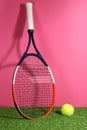 Tennis racket and ball on on green grass against pink background. Sports equipment Royalty Free Stock Photo