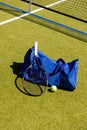 Tennis racket, ball and sports bag on the ground by net on sunny outdoor grass court, copy space Royalty Free Stock Photo