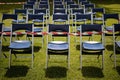 Tens of blue chairs seats lined outside in rows, front view. set on green grass. focal point on front chairs, whit red-white tape Royalty Free Stock Photo