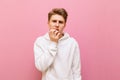 Tense young man in white hoodie isolated on pink background, looking into camera with worried look and biting finger nails. Royalty Free Stock Photo