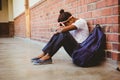 Tensed girl sitting against brick wall in school corridor Royalty Free Stock Photo