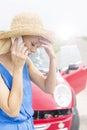 Tensed young woman using cell phone by broken down car