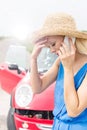 Tensed young woman using cell phone by broken down car