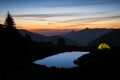 Tent glowing beside blue pond at sunset