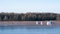 Tents and fishermen ice fishing on the blue ice of the lake on a clear frosty morning against the background of a winter forest Royalty Free Stock Photo