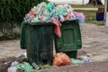 An overflowing trash can or garbage can with various plastic containers in an outdoor