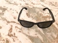 Ternary Sun-baked Plastic Glasses With Black Glass And Bows Lie On A Brown Sand-colored Light Stone With Multi-colored Mottled Sti