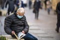 Man with medical mask reads a book outdoors