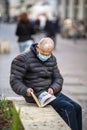 Man with medical mask reads a book outdoors