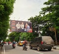 Motorcyclists and cars on the SULTAN ALAUDDIN road, and a banner with a picture of three doctors wearing masks