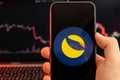 Terra LUNA cryptocurrency logo on the screen of smartphone in mans hand with downtrend on the chart on a red light Royalty Free Stock Photo