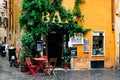 Terrace of a bar or cafe in the Trastevere of Rome, with red chairs and table. Warm tones and moisture shines on the floor.