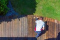 Terrace cleaning. Worker renovating a gray terrace using a hard scrub brush and green gel for renovating faded, gray boards