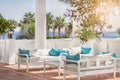 Terrace with columns, white benches with blue pillows by the sea and the palm alleys in a sunny day