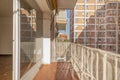 A terrace of a house with a white metal railing and with large glass and aluminum windows leading to an empty living room and a