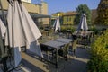 Terrace of restaurant on the rooftop across buildings. Platic tables and chairs, umbrellas in a garden across green trees and bush