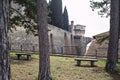 Terrace with trees and benches next to a boundary wall of a castle with a bridge in the distance