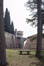 Terrace with trees and benches next to a boundary wall of a castle with a bridge in the distance