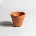 A terracotta flower pot sits on a white surface. The pot is empty, with a classic tapered Royalty Free Stock Photo