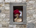 Terracotta sculpture of a young woman in a window wearing a red hat in Castellina in Chianti, Italy.