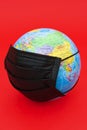 Terrestrial globe model with black surgical mask isolated on red background. Concept: Quarantined earth. Protection against Corona Royalty Free Stock Photo