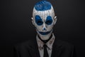 Terrible clown and Halloween theme: Crazy blue clown in black suit isolated on a dark background in the studio