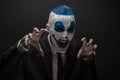 Terrible clown and Halloween theme: Crazy blue clown in black suit isolated on a dark background in the studio Royalty Free Stock Photo