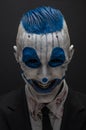 Terrible clown and Halloween theme: Crazy blue clown in black suit isolated on a dark background in the studio Royalty Free Stock Photo