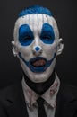 Terrible clown and Halloween theme: Crazy blue clown in black suit isolated on a dark background in the studio