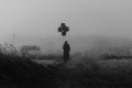 terrible man in a hooded cloak with balloons in his hand stands in a foggy field Royalty Free Stock Photo