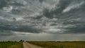 A terrible rain cloud hangs over an agricultural field and a dirt road. Hurricane and thunder over a green meadow. Climate change