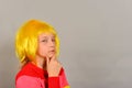 A terrible and serious girl in a yellow wig and bright colored clothes looks at the camera, a child on a gray background Royalty Free Stock Photo