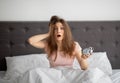 Terrified yound woman holding alarm clock in bed at home, grabbing her head, oversleeping to work Royalty Free Stock Photo