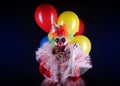 Terrifying clown with air balloons on dark background. Halloween party costume