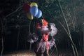 Terrifying clown with air balloons outdoors at night. Halloween party costume