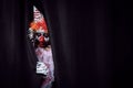 Terrifying clown hiding behind black curtains, space for text. Halloween party costume Royalty Free Stock Photo